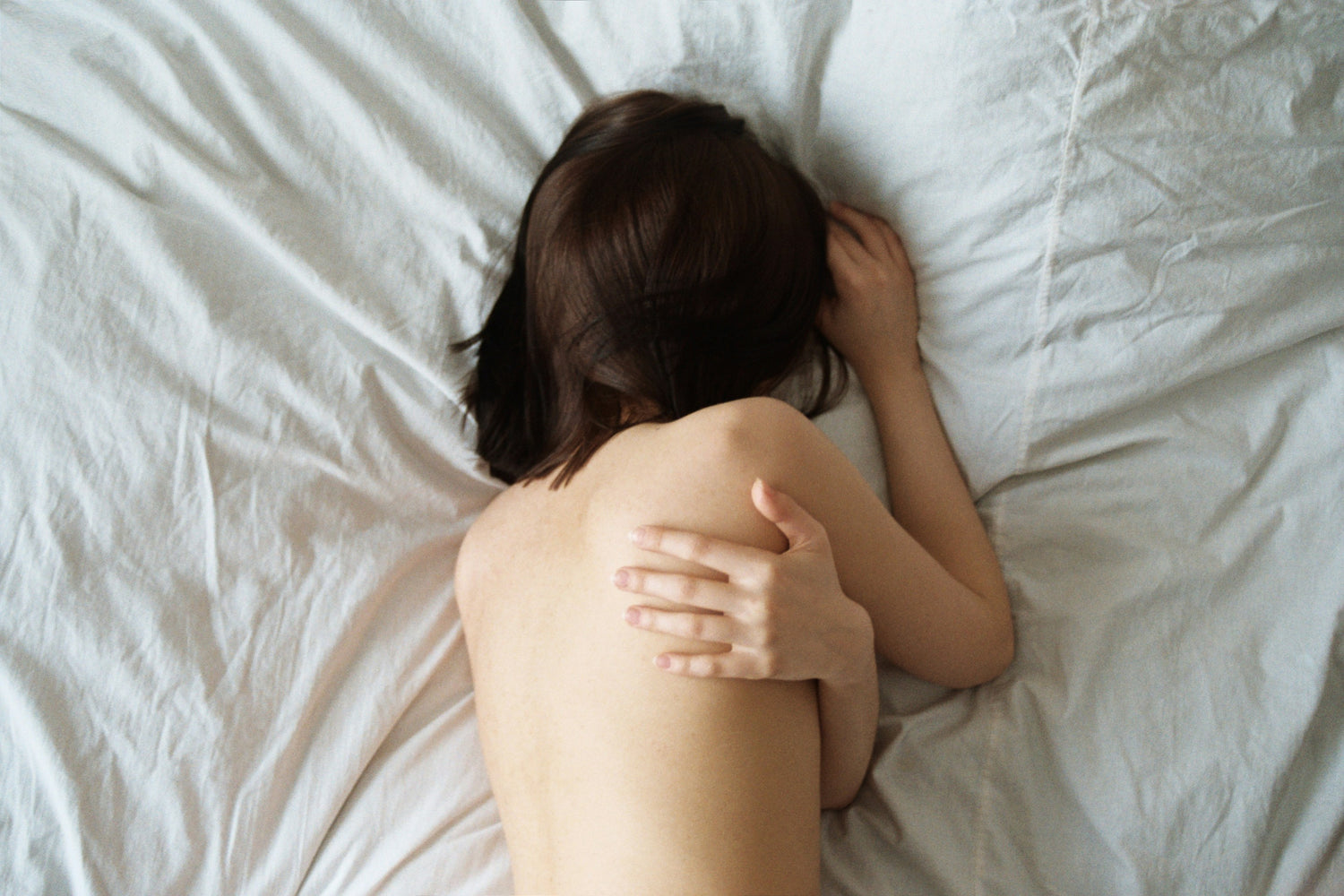 Photo d'une femme aux seins nus allongée sur son lit, montrant son dos en train de se détendre.