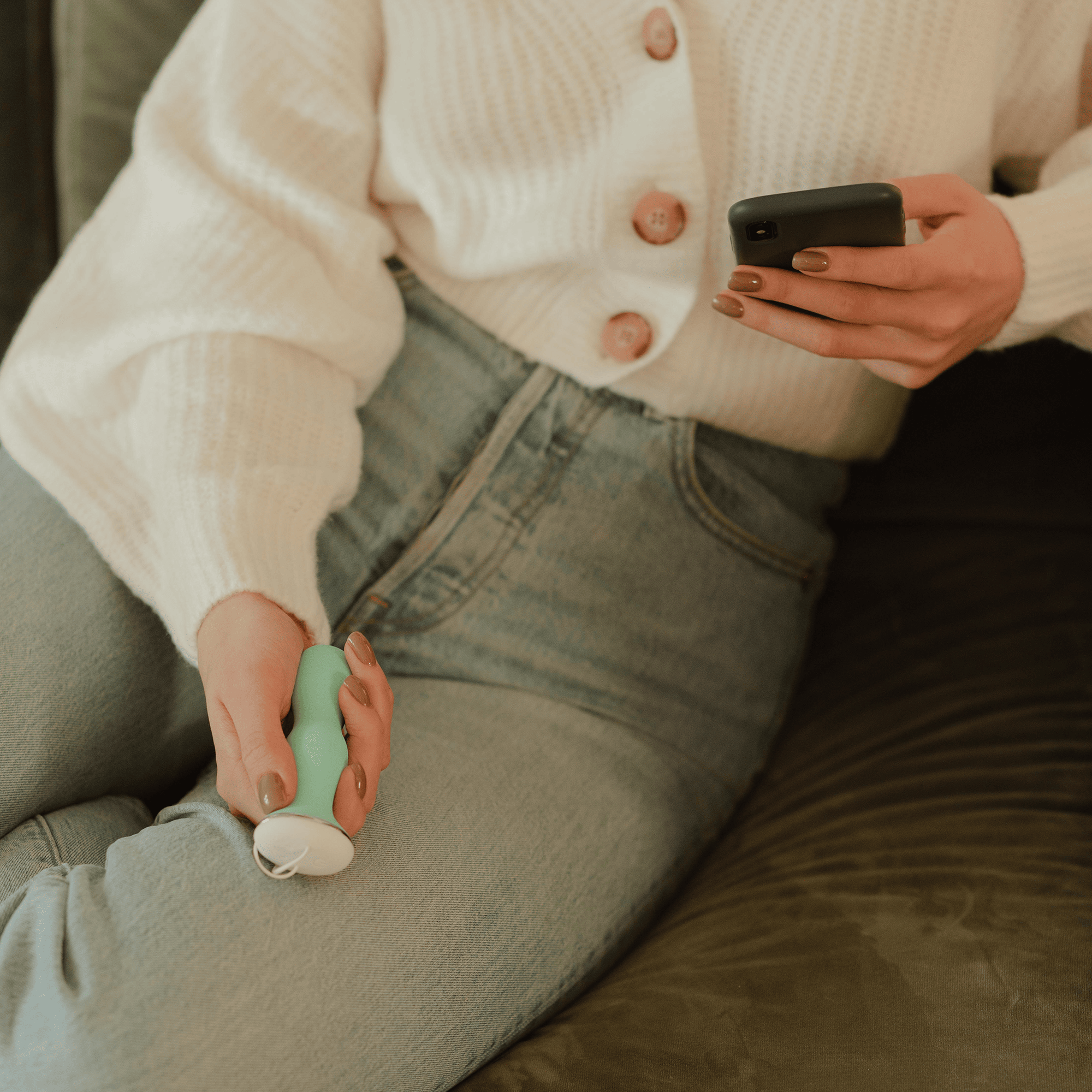 Woman in jeans holding Perifit in one hand and a smart phone in the other hand.